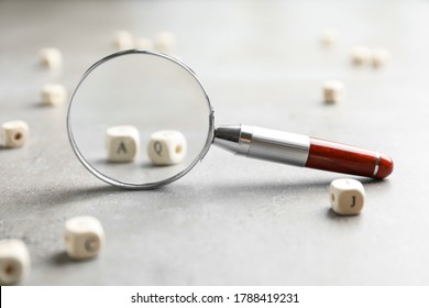 View on cubes with letters A and Q through magnifying glass at light grey stone background, closeup. Find keywords concept
