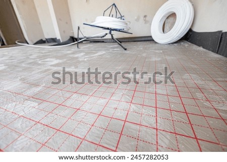 View on divided surface, with red auxiliary lines, grid, for help in placing pipeline of underfloor heating system in a residential building under construction.