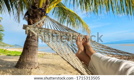 View on female feet in hammock under palm tree, swinging and relaxing  on a sand beach 