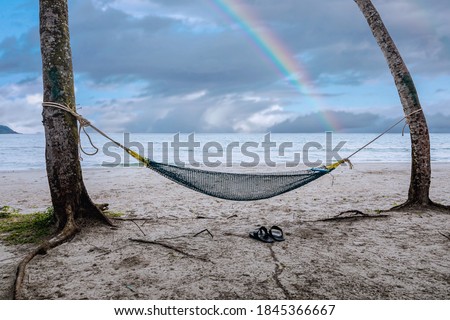 View on hammock between two palm trees on the beach with with rainbow colors after rain