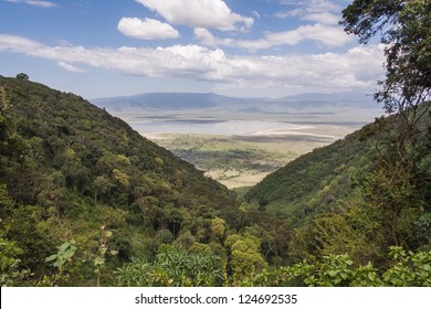 View on huge Ngorongoro caldera (extinct volcano crater) with large lake from cleft against blue sky background. Great Rift Valley, Tanzania, East Africa.