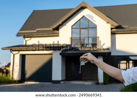 View on keys in hand in front of a new house, real estate investment concept. Buying or renting