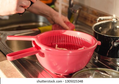 View On Kitchen Sink With Woman Hands Washing The Dishes With Water. A Pink Colander Is In Front. Cooking Process Concept.