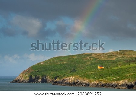 View on Mizen Peninsula in county Cork, Ireland. Colorful rainbow symbol of luck in the sky. Calm water of Atlantic ocean and green fields. Irish landscape. Popular travel destination. Nature wonder.
