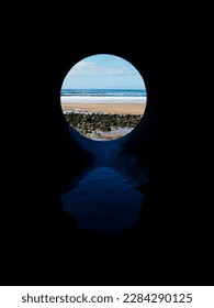 View on the ocean from a pipe or round shape hole with reflection inside the pipe. Abstract nature concept. Blue cool tone. Artificial framing of nature.