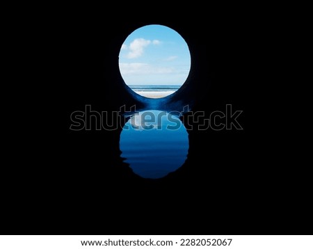 View on the ocean from a pipe or round shape hole with reflection inside the pipe. Abstract nature concept. Blue cool tone. Artificial framing of nature.