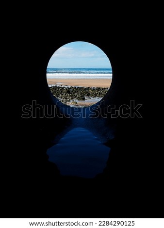 View on the ocean from a pipe or round shape hole with reflection inside the pipe. Abstract nature concept. Blue cool tone. Artificial framing of nature.