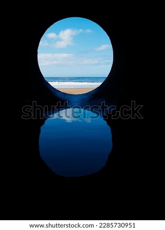 View on the ocean from a pipe or round shape hole with reflection inside the pipe. Abstract nature concept. Blue cool tone. Artificial framing of nature.