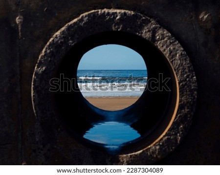 View on the ocean from a pipe or round shape hole with reflection inside the pipe. Abstract nature concept. Blue cool tone. Artificial framing of nature.