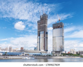 View on office business buildings under construction with working cranes on the roof on river side. Moscow-City business center area. Moscow skyscraper architecture. Blue clouds in the summer sky