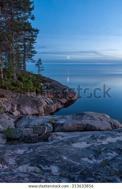 View on Onega Lake granite shore and\
evening glow with crescent reflecting in calm water at midnight\
sun. Besov Nos cape, Karelia Republic,\
Russia.\
