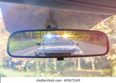 View on rear mirror of a car. Police car with lights and siren is chasing you.