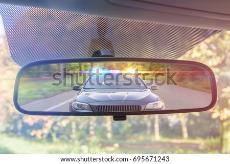View on rear mirror of a car. Police car with lights and siren is chasing you.