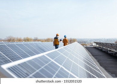 View on the rooftop solar power plant with two engineers walking and examining photovoltaic panels. Concept of alternative energy and its service - Shutterstock ID 1552051520