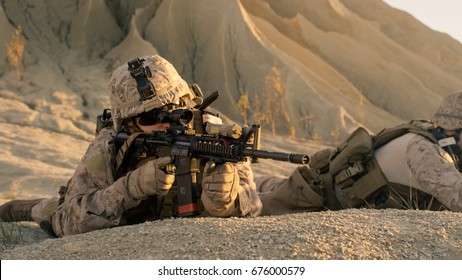 View On Soldier Lying Down On The Hill, Aiming Through The Assault Rifle Scope In Desert Environment.