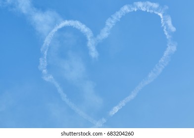 View On Sport Plane Vapour Trail In Shape Of Loving Heart. Made By Two Sport Planes White Vapour Trail Track On Blue Sky Background. Heart Shaped Plane Vapour Trail. Aerobatic Maneuver