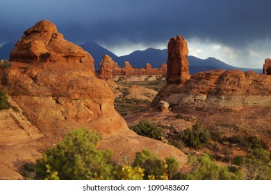 View on the sunlit red rocks and the stormy skies and mountains silhouette in the background in the Arches National Park, Utah - Shutterstock ID 1090483607