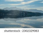 View on Woerthersee in Poertschach in Carinthia, Austria.The calm surface of the lake is reflecting the mountains, sunbeams and clouds. Clear and sunny day. Karawanks mountain range. Alps, Lake Woerth