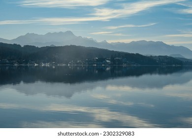 View on Woerthersee in Poertschach in Carinthia, Austria.The calm surface of the lake is reflecting the mountains, sunbeams and clouds. Clear and sunny day. Karawanks mountain range. Alps, Lake Woerth - Powered by Shutterstock