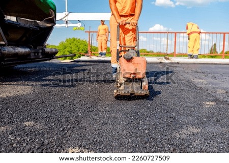 View on worker who is compacting asphalt with vibration plate, compactor machine on the bridge under construction.