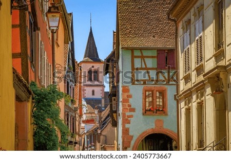 View onto a church tower and ornate traditional half timbered houses with blooming flowers in a village on the Alsatian Wine Route, Riquewihr, France