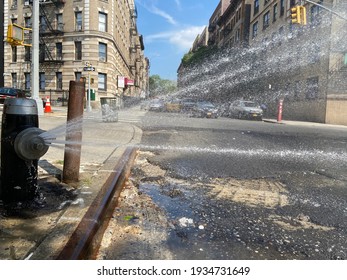 View of an open fire hydrant with cap spraying water onto the street on a hot summer day in New York, NY, USA