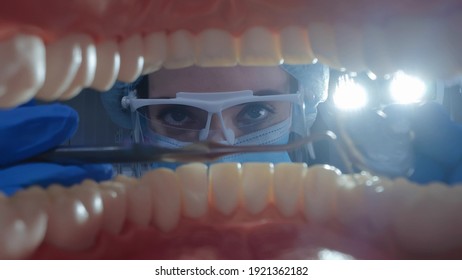 View From Open Mouth Of Female Dentist Examining Patient Teeth With Tools. Woman Orthodontist In Safety Mask, Goggles And Cap Checking Up Teeth Of Person In Dental Clinic