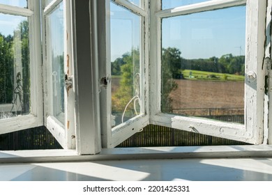 View From Open Window In The Village. White Old Wooden Windows With View On Blue Sky And Green Field. Symbol Of Insouciance, Freedom, Summer Atmosphere. Holiday House, Summer Cottage, Weekend Cottage.