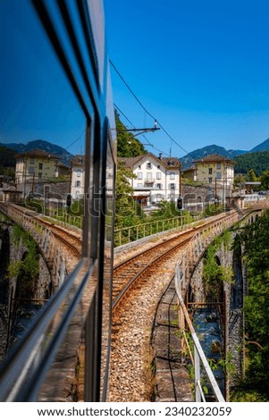 View out of a coach of the Centovalli railway, a popular electric narrow gauge train between Domodossola and Locarno. Passing a historic brick stone bridge and the swiss-italian border in Camedo.