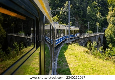 View out of a coach of the Centovalli railway, a popular electric narrow gauge train between Domodossola and Locarno, Switzerland. Passing a historic brick stone bridge near Coimo and Druogno, Italy.