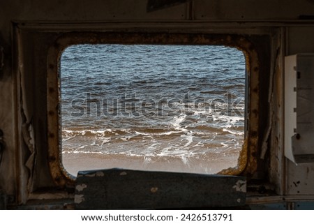 view out to sea, coast and waves through a port hole of an old abandoned fishing boat