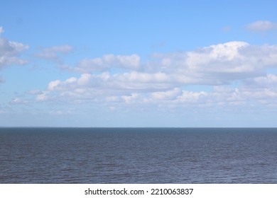 View Out To Sea With Pale Blue Cloudy Sky Above Dark Water