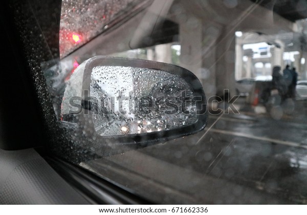 View outside car, rain drops at the car\
glass. Rain drops at the wing mirror\
car.
