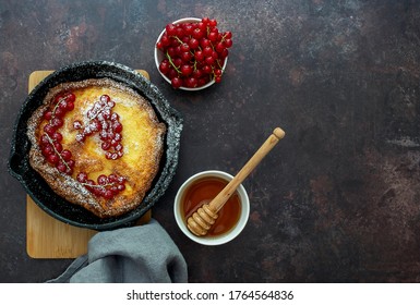 View Over Above Of Fresh-baked Dutch Baby Pancake In Iron Cast Pan Served Red Currant Berries, Maple Syrup, And Sugar Powder. Flat Lay, Copy Space.