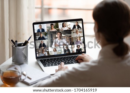 View over businesslady shoulder seated at workplace desk look at computer screen where collage of many diverse people involved at video conference negotiations activity, modern app tech usage concept