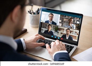 View over businessman shoulder at laptop where four multiracial colleagues engaged at group meeting on-line, video conference call communicating by webcam, distant webinar, online negotiations concept - Shutterstock ID 1694685169