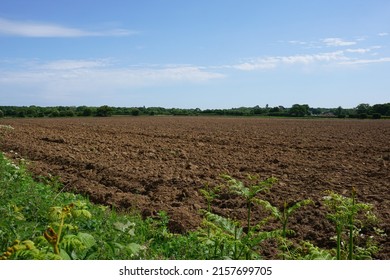 View over cultivated farm field.  Ploughed soil earth ready for growing crops. Brown farmland landscape in early summer 