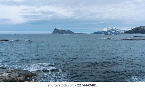 view over the ocean to steep mountain sides of the island Høya off Troms, rise out of the ocean from the North Atlantic. snowy mountains in colored morning light in Troms, northern Norway. 