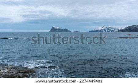 view over the ocean to steep mountain sides of the island Høya off Troms, rise out of the ocean from the North Atlantic. snowy mountains in colored morning light in Troms, northern Norway. 