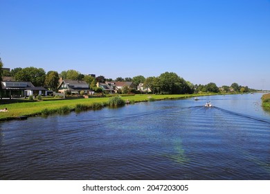 View over river Alblas on meadow with residential houses against blue cloudless clear summer sky - Alblasserdam, Netherlands (focus on houses left)
