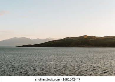 A View Over A Scottish Coastline From Across The Ocean At Sunset