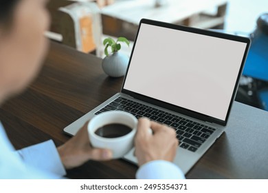 View over senior businessman shoulder holding cup of coffee and using laptop at cafe. - Powered by Shutterstock