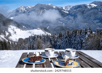 View over a set table with coffee and cake to the Chiemgau Alps and Geigelstein (1808 m), Bavaria, Germany in winter.