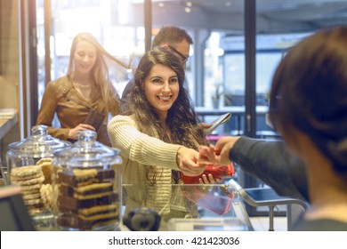 View Over The Shoulder Of The Cashier Of An Attractive Young Blond Woman Making Payment At A Till Looking In Her Purse