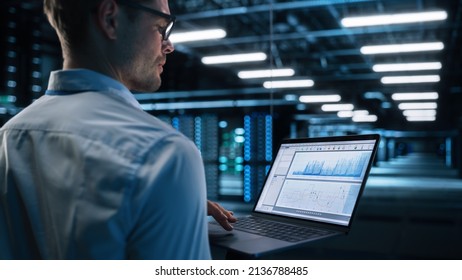 View Over the Shoulder of Caucasian Data Center IT Technician Standing at the Corridor with a Laptop Computer with Chroma Key Screen. Chroma Key Desktop Computer at the Programmer Hands