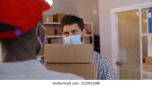 View Over Shoulder Of Courier In Mask Give Package To Distribution Warehouse Worker. Delivery Office Manager Wearing Protective Mask Receive Parcel From Deliveryman