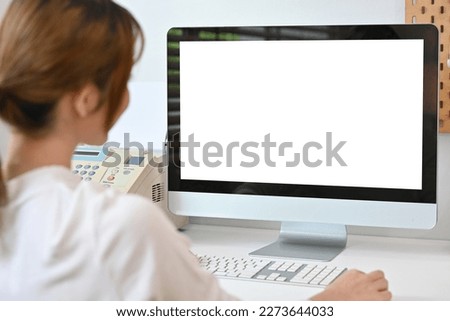View over shoulder of young creative woman looking at white blank computer monitor.