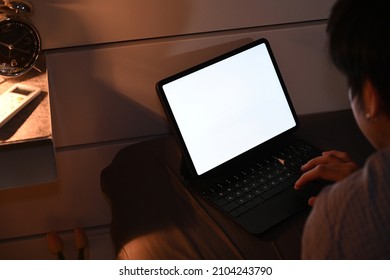 View over shoulder young man lying in bed and working with computer tablet at night.