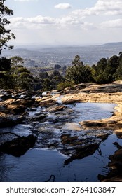 View over a small stream flowing the ancient rocks of the Piggs Peak region of Eswatin, with lowveld stretching in the distance in the background.