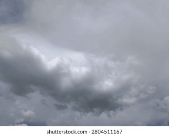 A view of an overcast sky filled with dense, grey and white clouds. The clouds vary in shade, with darker, heavier formations dominating the lower portion and lighter, thinner clouds above. A small, brighter area suggests the sun is hidden behind the thick cloud cover.